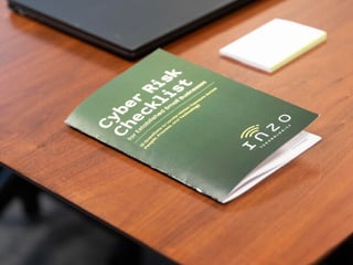 Inzo Technologies Cyber Risk Checklist booklet on a wooden conference table, with a laptop and sticky notes in the background.