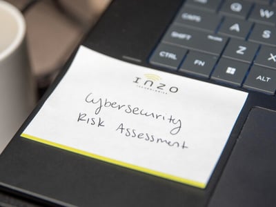 Inzo Technologies notepad with “Cybersecurity Risk Assessment” handwritten on it, resting on a laptop keyboard