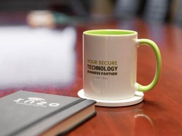 Close-up of an Inzo Technologies branded mug with green handle and interior on a conference table, beside a blurred notebook.