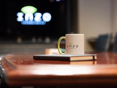 Inzo Technologies mug with green handle sitting on a notebook on a conference table, with a blurred Inzo logo in the background.