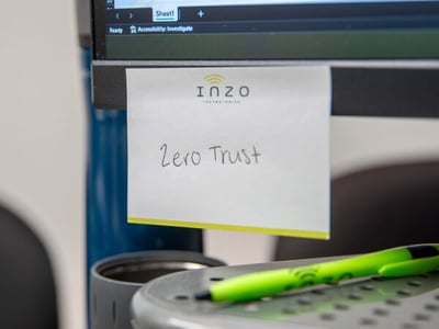 Inzo Technologies notepad with “Zero Trust” handwritten on it, attached to a computer monitor above a desk